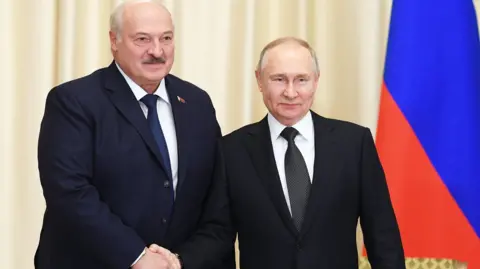 KREMLIN POOL O presidente da Bielo-Rússia, Alexander Lukashenko, vestindo terno escuro, camisa branca e gravata azul escura, aperta a mão do presidente russo, Vladamir Putin, que usa terno escuro, camisa branca e gravata preta. Uma bandeira russa pode ser vista à direita da foto.