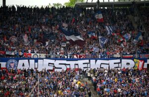 Torcedores do Holstein Kiel no jogo em Hannover 96 em 19 de maio de 2024 com um "Estrela em ascensão"-Bandeira.