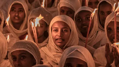 AFP Mulheres cristãs ortodoxas usando lenços brancos na cabeça e segurando velas em orações antes das celebrações de Natal na Igreja Bole Medhanialem em Adis Abeba - 6 de janeiro de 2024