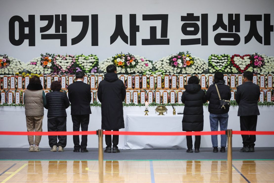 Pessoas em luto diante de um altar memorial às vítimas do acidente aéreo de Jeju no Aeroporto Internacional de Muan, no parque esportivo Muan em Muan, Coreia do Sul, em 30 de dezembro de 2024.