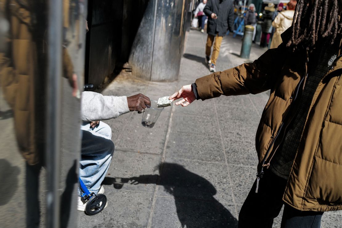 Um pedestre dá uma nota de um dólar a um sem-teto em 19 de março em Nova York.