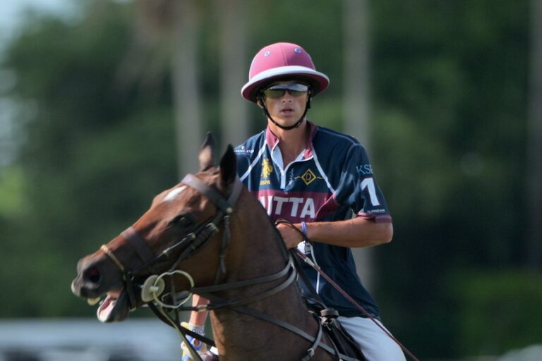 Um homem é visto cavalgando virando a cabeça para a direita com a boca aberta, o que parece ser uma partida de pólo.