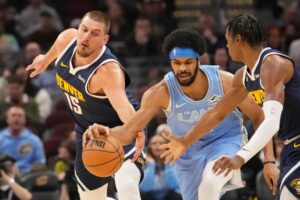 O pivô do Denver Nuggets, Nikola Jokic (15), o pivô do Cleveland Cavaliers, Jarrett Allen, o centro, e o atacante Peyton Watson, à direita, alcançam a bola no primeiro tempo de um jogo de basquete da NBA, quinta-feira, 5 de dezembro de 2024, em Cleveland. (Foto AP/Sue Ogrocki)