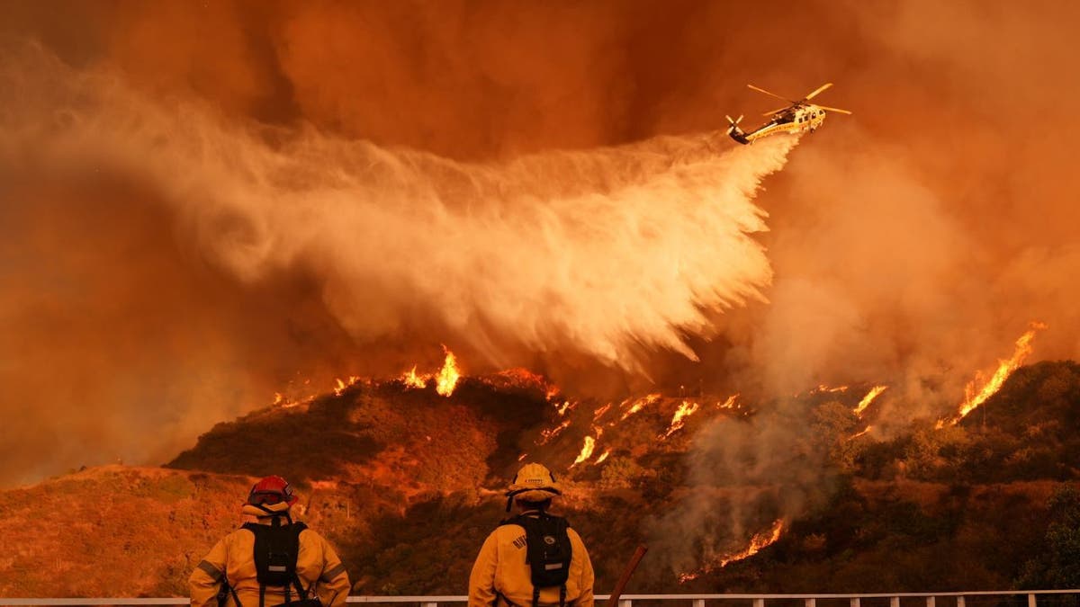 Os bombeiros assistem a um helicóptero cair água no incêndio em Palisades em Mandeville Canyon, em Los Angeles, no sábado, 11 de janeiro de 2025. (AP Photo/Jae C. Hong)