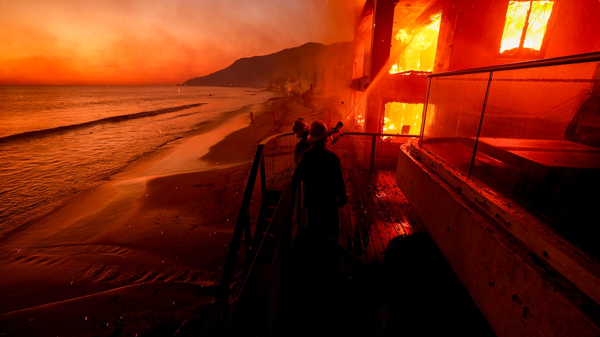 Os bombeiros trabalham de um baralho enquanto o incêndio de Palisadas queima uma propriedade à beira -mar