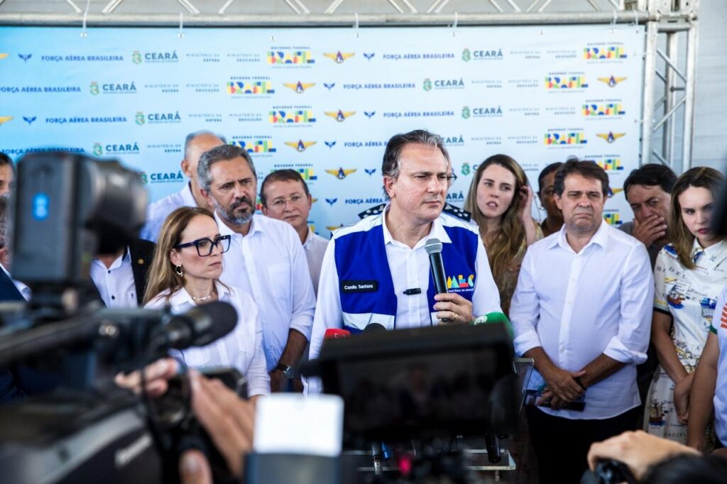 Camilo Santana segurando microfone, com várias autoridades ao seu lado, em entrevista coletiva à imprensa